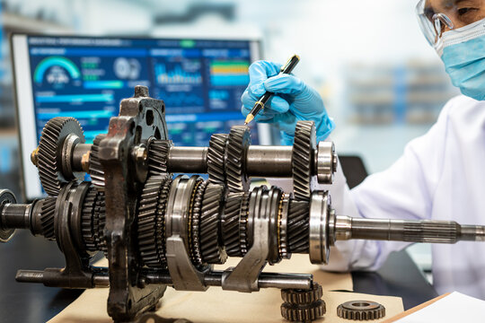 Automotive technician in protective mask and gloves inspects a manual transmission gearbox with a tool in a modern repair workshop.