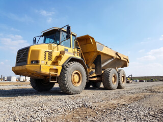Fototapeta premium Large yellow dump truck parked on gravel construction site under