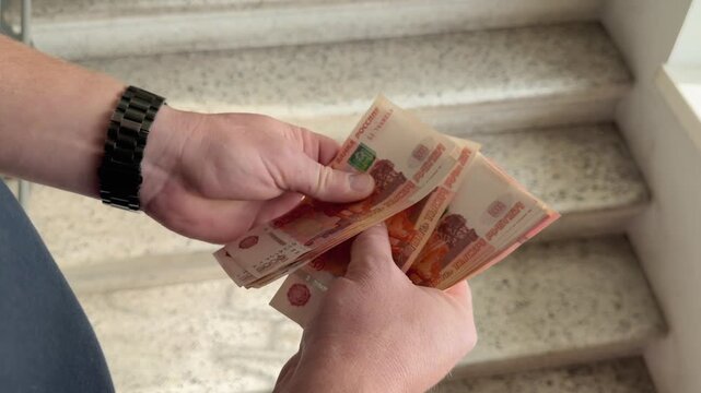 Man hands counting a large pack of five thousand rubles cash banknotes close up. This is a lot of paper money. Successful deal or loan payment process on the stairs. Financial budget wealth income. 