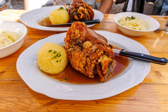 Traditional Bavarian crispy roasted pork knuckle Schweinshaxe served with potato dumpling and sauerkraut on wooden table, German beer garden cuisine concept