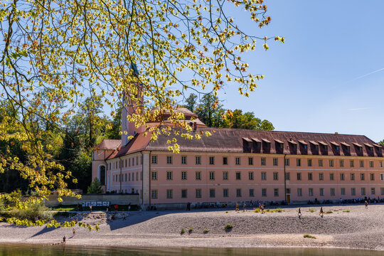 Historic Weltenburg Abbey Benedictine monastery building with pink facade on Danube River gravel bank framed by spring tree branches near Kelheim Bavaria Germany