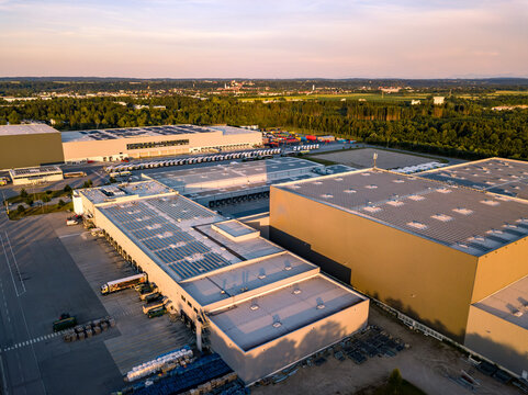 Aerial drone view of modern industrial logistics center warehouse and distribution hub with solar panels on roof at sunset, global supply chain and freight transportation concept