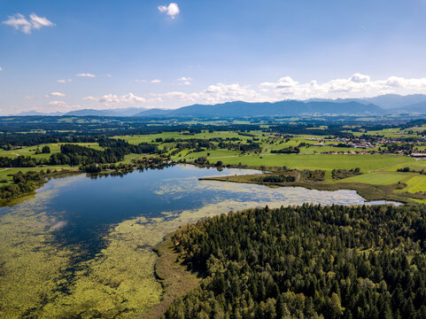 Aerial drone view of Haslachsee lake near Bernbeuren and Auerberg with dense forest and Bavarian Alps in background, German countryside and alpine landscape concept