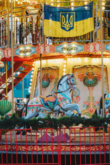 Colorful ornate carousel horse spinning on bright illuminated ride. Blue yellow trident flag. © reddish
