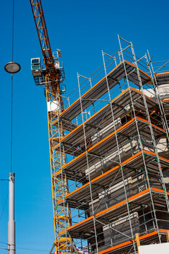 High tower construction crane operating next to extensive multi story metal scaffolding structure on modern residential building site against deep blue sky