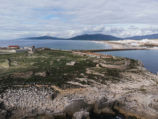 Aerial view of Isla de las Palomas, ancient stone ruins and fortifications on a coastal peninsula overlooking a bay with white town and mountains in Tarifa, Spain © Felix Morion