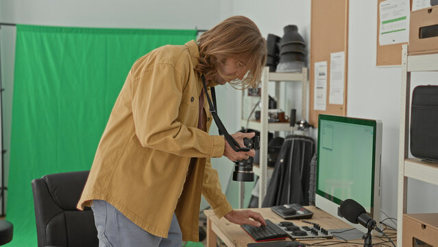 Man adjusts dslr camera and tweaks audio mixer and keyboard controls at desk in studio; focused creativity production.