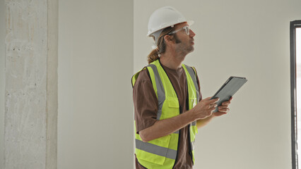Man architect in hardhat and vest holding tablet and checking plans inside building  planning concentration. © Krakenimages.com