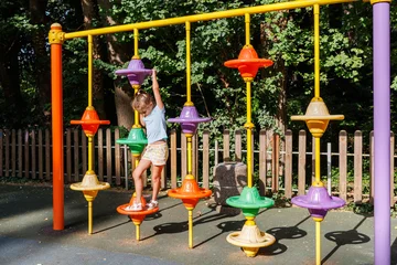 Happy Girl Playing on Colorful Playground Equipment in Sunny Park, Active Childhood and Outdoor Fun © dechevm