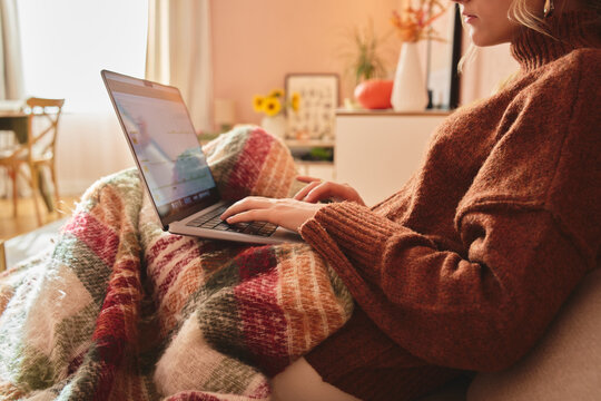 Woman using laptop under blanket at home.