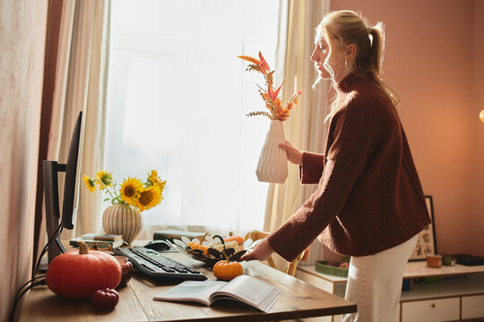 Woman decorating sunny home office for autumn.