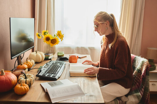 Woman studying at cozy autumn home office desk.