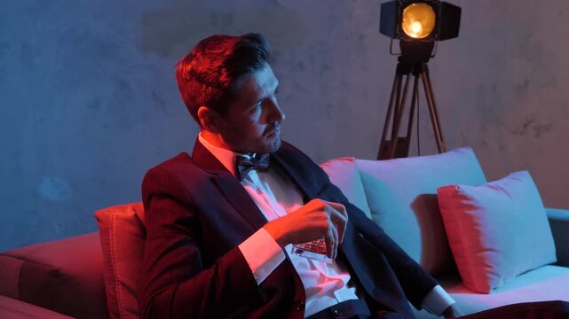 Man in checkered suit lounges on plush sofa in blue and orange studio lighting, relaxed corporate portrait