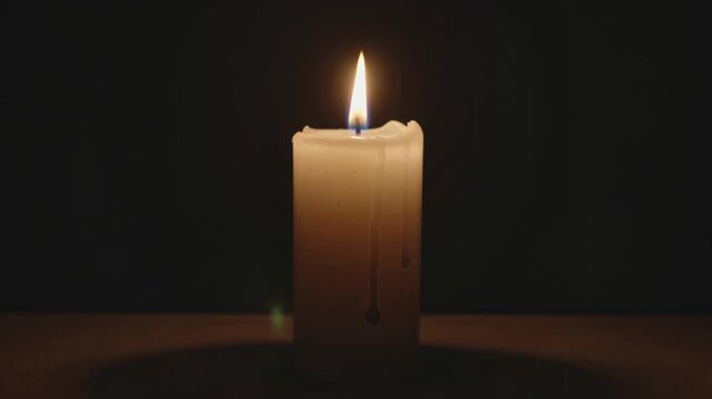 Cinematic video of a single white candle burning with a steady warm flame and melted wax against a deep dark background.