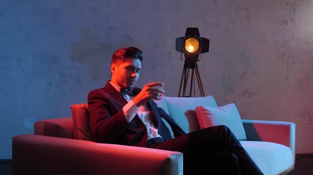 Man in suit sipping drink while seated on modern sofa under dual-tone studio lighting and tripod lamp accent