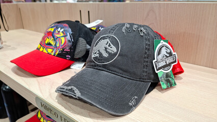 Fototapeta premium jurassic world washed grey distressed baseball cap with embroidered t rex logo on wooden retail shelf next to spider man hat on September 16, 2026 in Bangkok, Thailand.