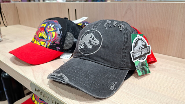 jurassic world washed grey distressed baseball cap with embroidered t rex logo on wooden retail shelf next to spider man hat on September 16, 2026 in Bangkok, Thailand.