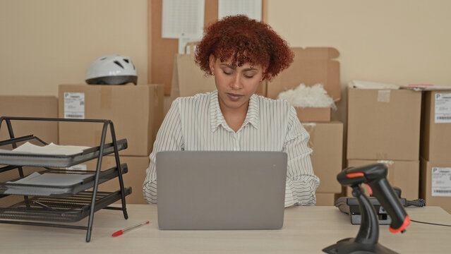Woman closes laptop and stretches hands at a packing desk in a building surrounded by cardboard boxes, tray and barcode scanner; relief efficiency.