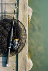 Fototapeta premium Leisure and recreation, fishing rod with net on wooden pier by lake for outdoor hobby and travel lifestyle, summer vacation activity at water edge