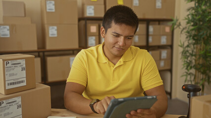 Man taps tablet while surrounded by shipping boxes at a packing desk inside a building  focused entrepreneurship. © Krakenimages.com