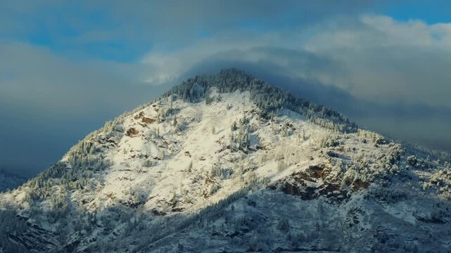 4K Landscape shot of snow covered Himalayan mountain peak after fresh snowfall during the winter season with clouds surrounding it as seen from Manali in Himachal Pradesh, India. Winter background.