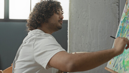 Man painter wearing apron holds palette and brush and paints bold strokes on canvas in studio  focused concentration. © Krakenimages.com