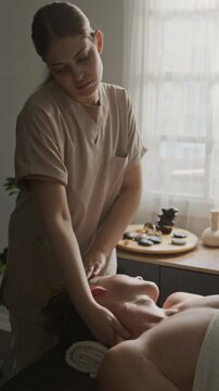 Vertical video of young adult Caucasian female masseuse massaging neck of client during spa treatment. Useful for wellness clinic marketing, body care campaigns, or holistic health advertising