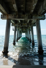 Fototapeta premium Travel and vacation escape, wooden pier structure over ocean waves with perspective view and sunlight reflection on water surface at tropical beach