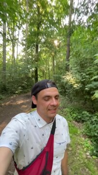 man walks along narrow dirt path in dense deciduous woods, sun rays glowing through leaves, warm shadows on ground, outdoor hiking mood today in peace calm