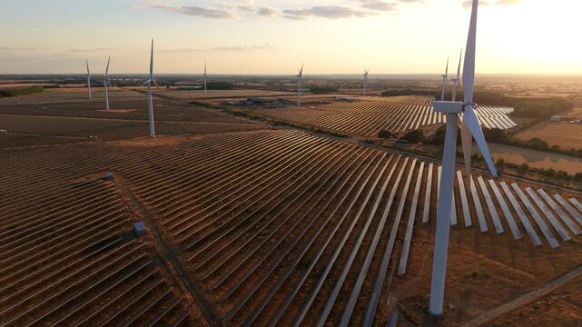 Hybrid solar farm and wind turbines at golden hour sunset in an aerial view in Chelveston, UK
