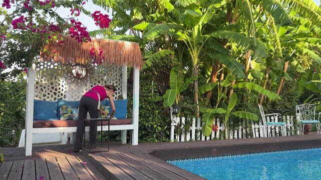Mujer limpiando y organizando cama balinesa junto a piscina