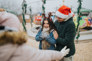 Naklejka premium Young couple wearing Santa hat and reindeer antlers share a warm hug at a winter fair. A festive scene at an outdoor amusement park with holiday decorations and smiles.