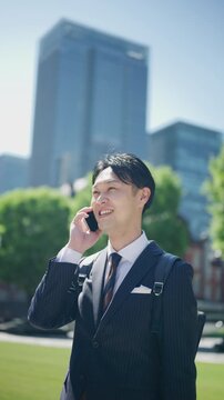 Japanese businessman talking on a smartphone in front of office towers in Tokyo