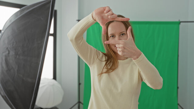Woman framing with hands and smiling toward camera beside a softbox light and green screen backdrop in a studio; creative intent.