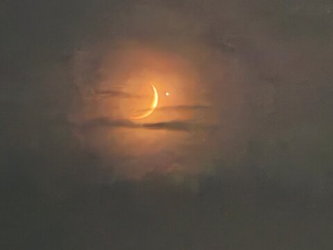 Crescent moon and Venus planetary conjunction glowing through night clouds