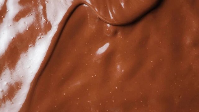 Glossy liquid chocolate wave creeping over smooth background slow motion macro