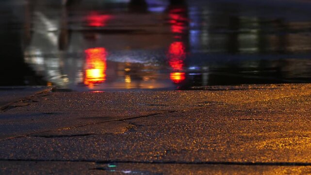 Close up shot of wet road asphalt surface at night with golden light reflections from traffic, cars driving, and pedestrians walking in rainy city evening stock video.