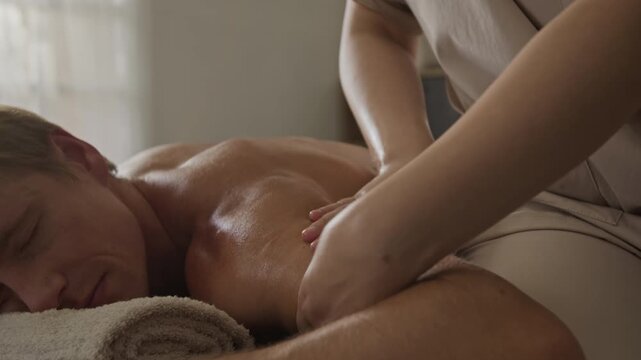 Professional therapist massaging shoulder and arm of Caucasian adult man during bodywork session. Footage suitable for spa advertising, physiotherapy promotion and wellness campaigns
