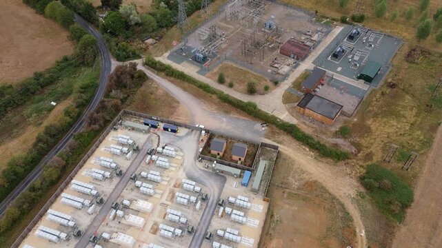 Close aerial flyover of modular battery energy storage units and high-voltage 400kV electrical substation equipment in Stony Stratford, UK