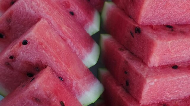 Close-up shot of juicy red watermelon slices stacked together, rotating smoothly to reveal rich red pulp texture and black seeds, perfect for culinary and summer content.