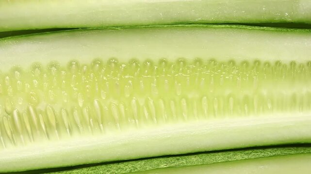 Fresh long cucumber sliced lengthwise showing flesh texture, slowly rotating. Top view shot