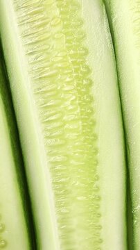 Fresh long cucumber sliced lengthwise showing flesh texture, slowly rotating. Top view shot