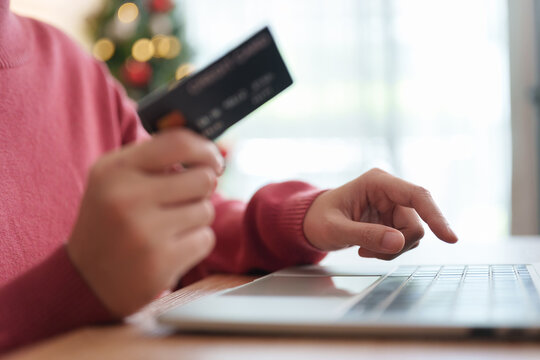Woman holding credit card while shopping online on a laptop during Christmas, representing digital payment, e-commerce checkout, holiday purchases and  seasonal sales.