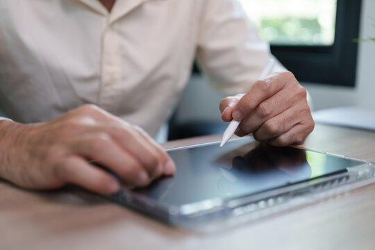 Businessman using a stylus on digital tablet at a desk, representing modern business, touchscreen technology, digital writing, productivity, mobile work and professional workflow.