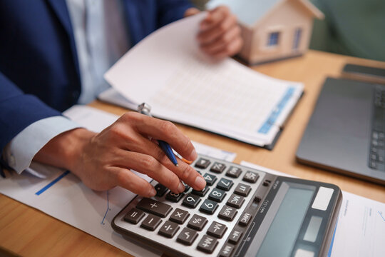 Businessman using a calculator while reviewing mortgage documents beside laptop, representing home loans, property finance, housing costs, budgeting and repayment planning.