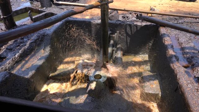 Close up of long metal bailer pipe extracting crude oil with splash at Wonocolo traditional oil well, Bojonegoro, East Java, Indonesia. Traditional petroleum extraction and heritage mining process.