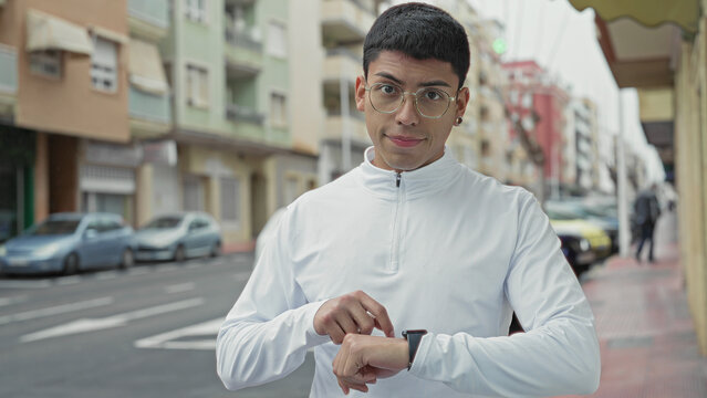 Man tapping smartwatch on wrist on street with parked cars and apartment buildings visible; punctuality focus.