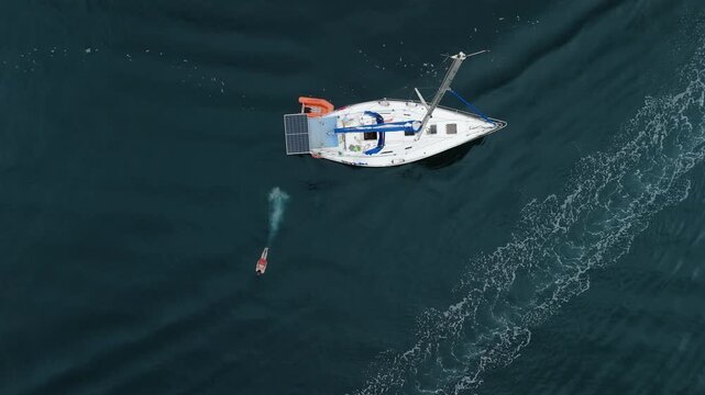 Aerial view of the sailing boat in the calm sea. Man jumps from the boat and swims in the water nearby