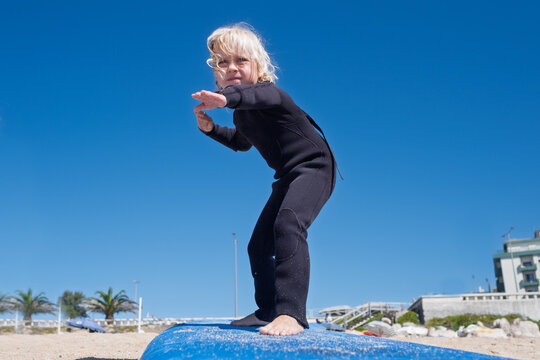  girl in black wetsuit practicing surf balance on board at sandy beach