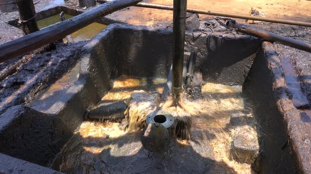 Close up of long metal bailer pipe extracting crude oil with splash at Wonocolo traditional oil well, Bojonegoro, East Java, Indonesia. Traditional petroleum extraction and heritage mining process.